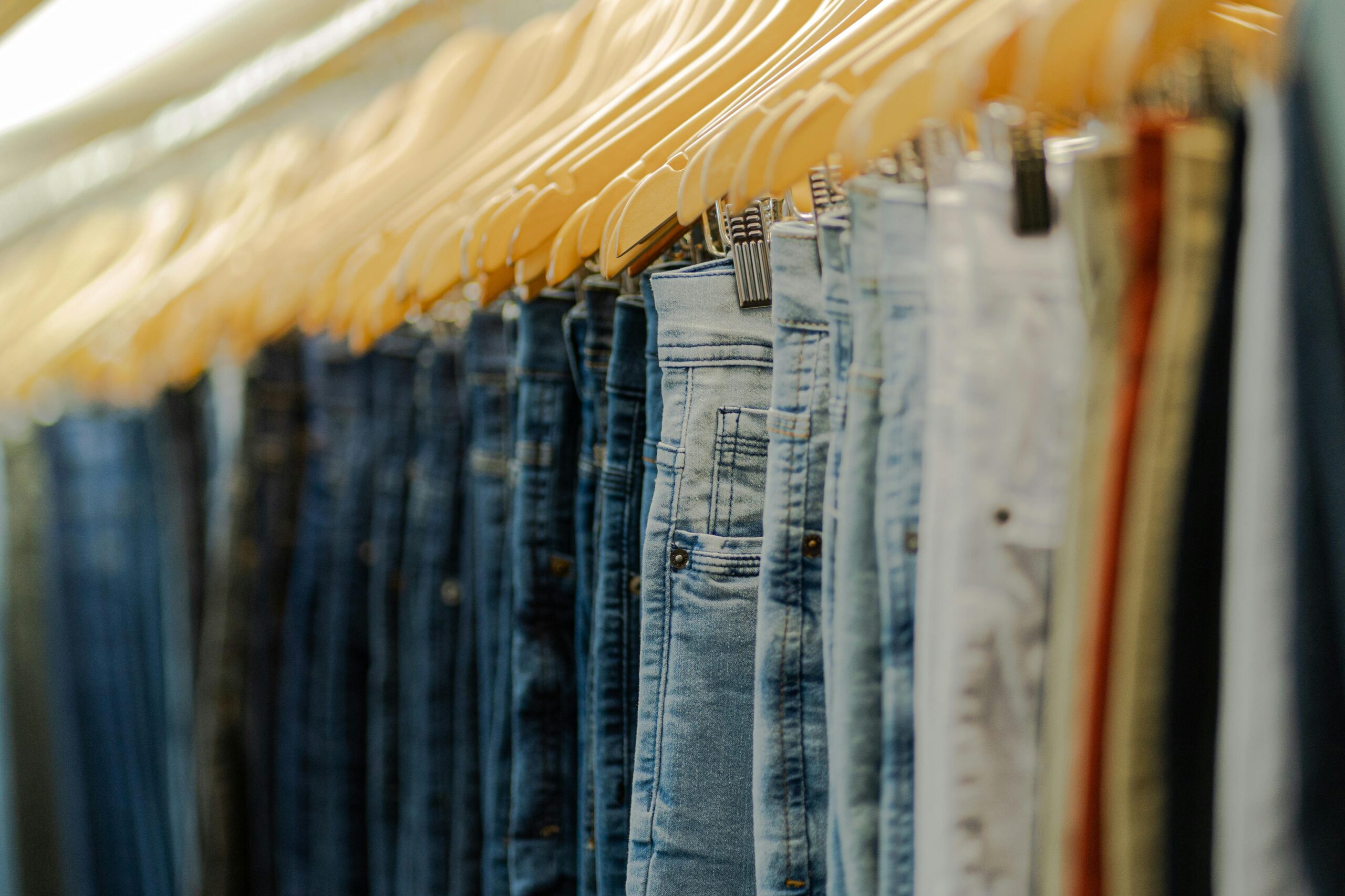 A close-up view of various denim jeans hanging on wooden hangers showcasing fashion style.